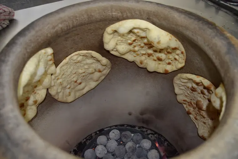 Flatbread baking against the wall of a clay tannour oven