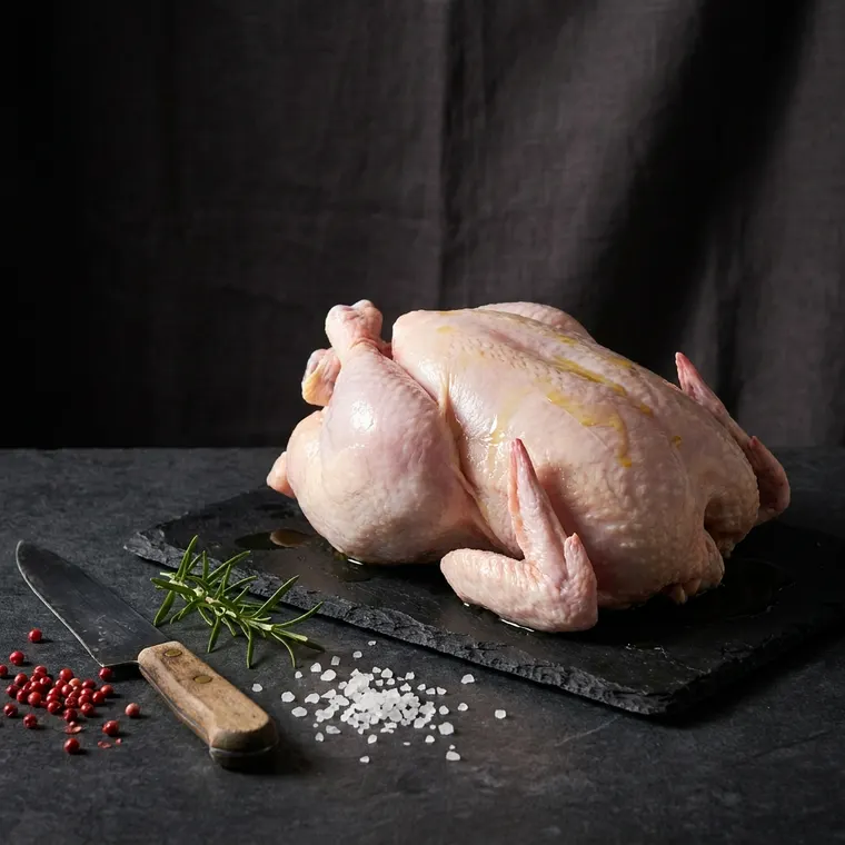 A whole fresh chicken on a dark slate board
