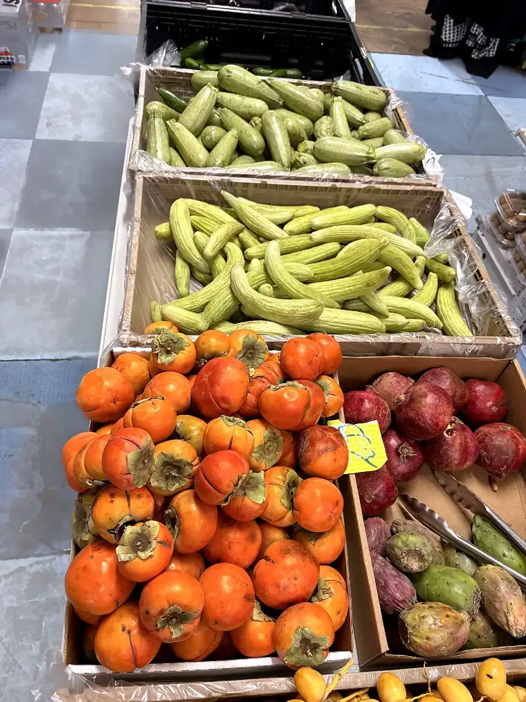 Crates of persimmons, cucumbers, courgettes and pomegranates on the produce table