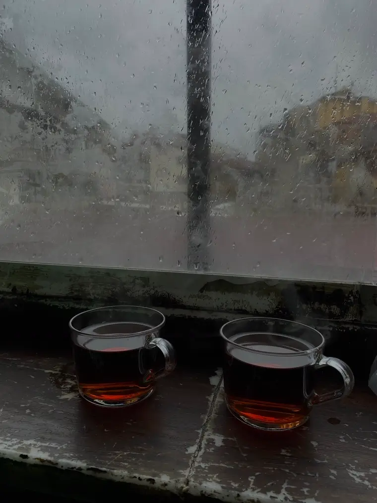 Two glasses of black tea on a sill against a rainy window